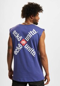 Sleeveless purple cotton tank top featuring bold white text and a red graphic accent on the back. Simple, relaxed fit with a smooth texture.