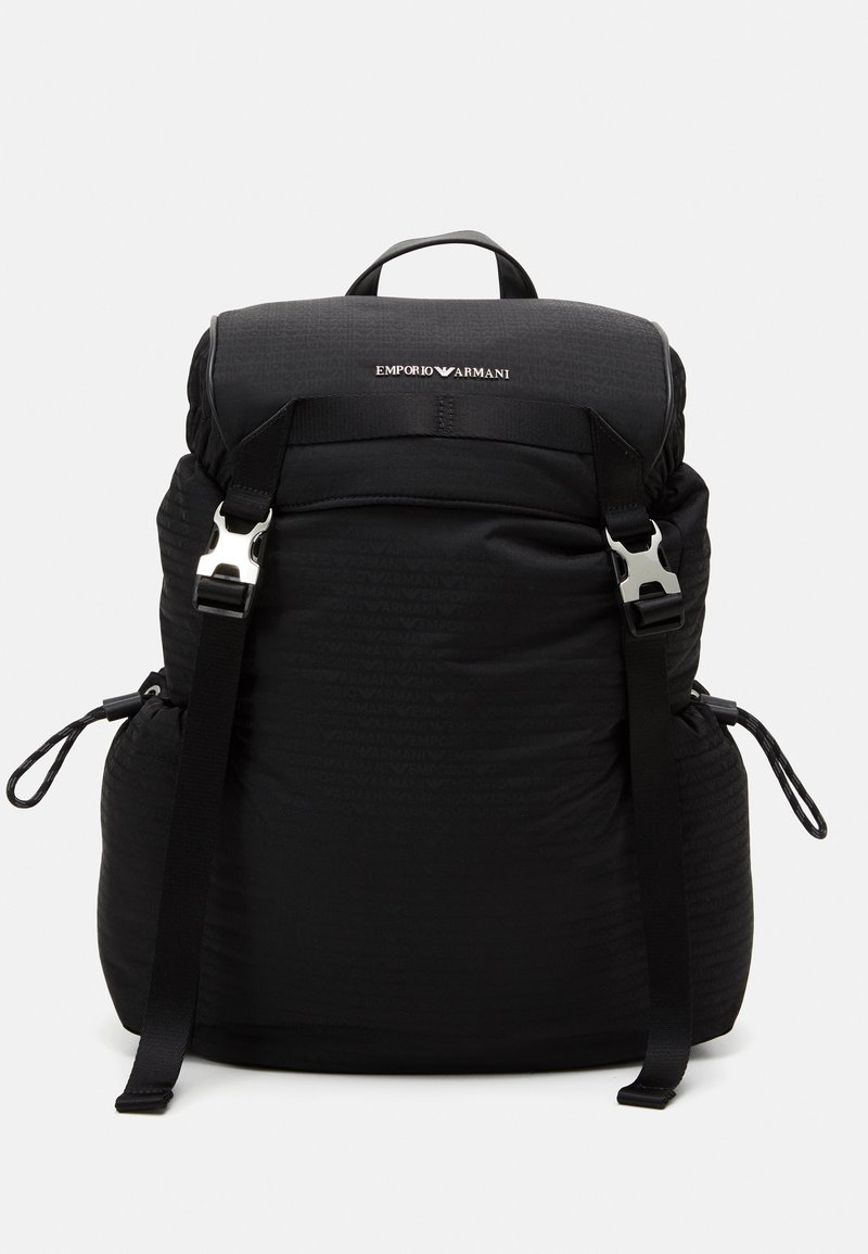 Zaino nero con parte superiore imbottita, spallacci regolabili e accessori in metallo. Presenta un logo in rilievo e una chiusura con cordoncino, realizzato in tessuto testurizzato.