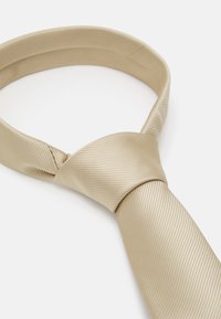 Corbata de seda beige con un sutil patrón de rayas diagonales, que presenta una textura suave y un estilo de nudo clásico.