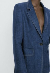 Laivasilmäinen bleiseri, joka on valmistettu teksturoidusta kankaasta ja jossa on lovettu kaulus, yksittäinen nappisulkeminen ja kontrastivalkoiset stitching-taskuissa.