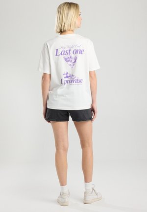 Witte katoenen T-shirt met een paars grafisch ontwerp op de achterkant, met tekst en een illustratie van een martini glas. Korte mouwen en een relaxed fit.