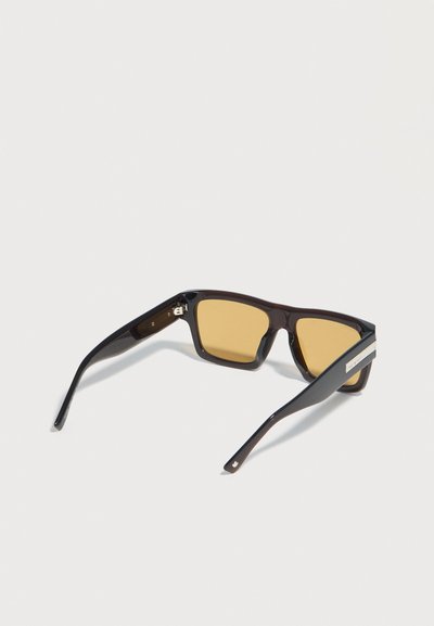 Μαύρα ορθογώνια γυαλιά ηλίου με κεχριμπαρένιους φακούς και ασημένιο λογότυπο μάρκας στα πλαϊνά, εμφανίζονται από πίσω γωνία σε λευκό φόντο.