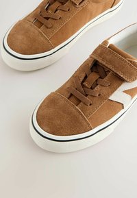 Baskets en daim marron avec semelles en caoutchouc blanc, lacets marron, une bride Velcro sur une chaussure, et un motif d'étoile blanche sur le côté.