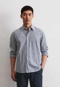 Striped button-up shirt in light blue and white cotton, featuring long sleeves rolled up, classic collar, and white buttons.