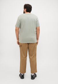 Mintgrønn t-skjorte med korte ermer og khaki cargo bukser med sidelommer, parret med svarte joggesko. Enkle farger, ledig passform.