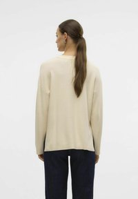 Beige ribbet sweater med en afslappet pasform, der har lange ærmer og en rund kant, parret med mørkeblå jeans. Glat tekstur.
