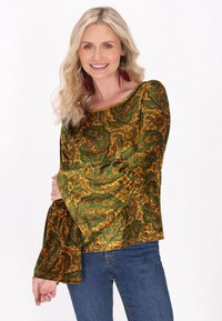 Top verde e oro con motivo paisley, maniche a campana e scollatura a patrizia, abbinato a jeans blu. Il tessuto ha una texture liscia.