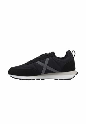 Zapatilla negra con diseño de X gris en el lateral, entresuela blanca, suela negra, cordones negros y cinta de tirón en el talón, mostrada en perfil derecho.