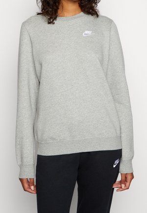 Osoba nosząca jasnoszarą bluzę Nike i czarne spodnie dresowe Nike, oba z białymi logo Nike.