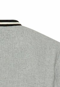 Graue Jacke mit texturiertem Finish, ausgestattet mit einem schwarz-weißen gestreiften Rippkragen. Die Rückseite zeigt ein schlichtes, unverziertes Design.