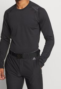 Svart långärmad träningströja med rund halsringning, med en subtil Adidas-logotyp på axeln och en figurnära design. Matchas med svarta byxor.