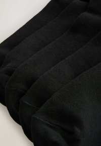 Vier Paare schwarze Knöchelsocken eng auf einem hellen Hintergrund gestapelt, wobei der Zehen- und Fußbereich sichtbar ist.