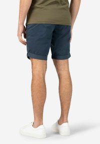 Marineblaue Baumwollshorts mit umgeschlagenen Säumen, kombiniert mit weißen Sneakers. Die Shorts verfügen über eine Seitentasche mit einem kleinen Logodetail.