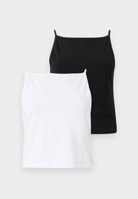 Deux camisoles sans manches à fines bretelles, une blanche à l'avant et une noire derrière, présentées sur un fond uni.