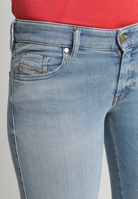Jeans de mezclilla azul claro con un ligero desgaste, que cuentan con cinco bolsillos, un cierre de botón metálico y detalles de costura a lo largo de las costuras.