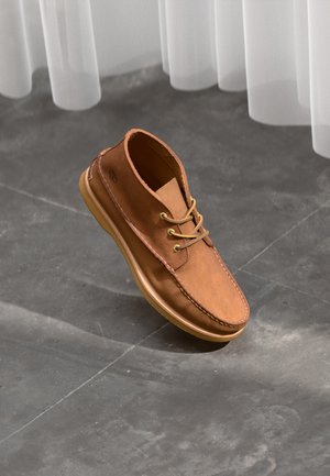 Brune lærstøvle med en glat overflade, rund tå og snørebåndsdesign. Har en gummisål og syninger langs kanterne.