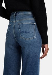 I jeans in denim blu presentano una vita a media altezza, gamba dritta, due tasche posteriori e un design di cucitura sottile. Il tessuto ha un aspetto morbido e testurizzato.