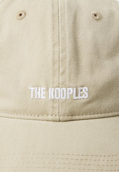 Casquette de baseball beige en tissu texturé, avec le texte brodé en blanc "THE KOOPLES" sur le devant et un bouton sur le dessus.