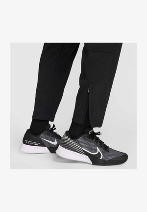 Os ténis Nike em preto e cinza apresentam um upper em malha, detalhes brancos e uma sola texturizada. O design inclui um padrão listrado distinto no calcanhar.