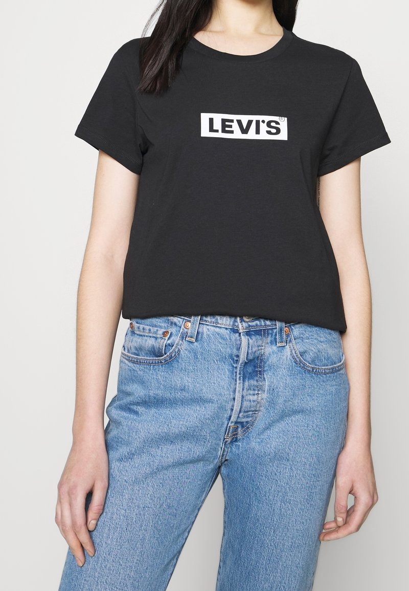 Černé bavlněné tričko s krátkým rukávem, zdobené bílým logem "LEVI'S" v obdélníkovém rámečku na hrudi. V kombinaci se světle modrými džíny.