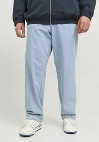 Jeans din denim de un albastru deschis, cu o croială lejeră și o textură subtilă, asortați cu adidași albi și blue. Materialul pare moale și casual.