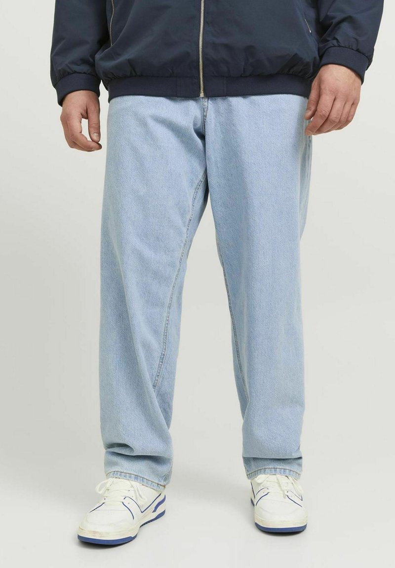 Jeans din denim de un albastru deschis, cu o croială lejeră și o textură subtilă, asortați cu adidași albi și blue. Materialul pare moale și casual.