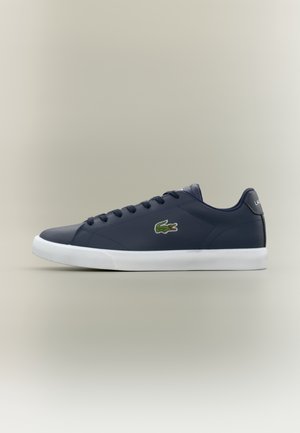 Baskets basses bleu marine avec semelle blanche, lacets foncés et logo crocodile vert sur le côté, vues de profil sur fond neutre.
