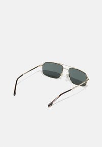 Goldene Metall-Sonnenbrille mit dunkelgrauen Gläsern, hexagonaler Form, dünnen Bügeln und einem Schildpatt-Muster an den Enden der Bügel.