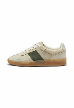 Low-top beige sneaker with white laces, green suede side panel, and gum sole, showing right outer side.