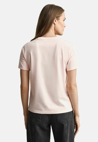 Rosa Baumwoll-T-Shirt mit Rundhalsausschnitt und kurzen Ärmeln, mit lockerer Passform und glatter Textur. Kombiniert mit schwarzen, hochtaillierten Hosen.