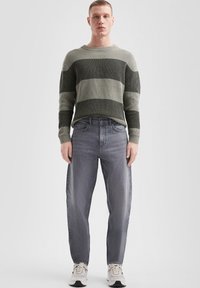 Sweter dziergany w zielone i szare poziome paski, w połączeniu z jasnoszarymi dżinsami i kremowymi sneakersami. Płaska tekstura i luźny krój.