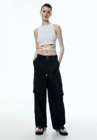 Witte geribde crop top met gekruiste banden, gecombineerd met losse zwarte cargobroeken met zijzakken en een riem met een ronde gesp.