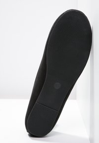 Czarna, płaska podeszwa buta z delikatnymi poziomymi rowkami, rozmiar 40 oznaczony na środku, ustawiona pionowo na białym tle w kącie.