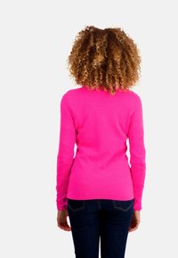 Un pull rose ajusté avec des manches longues, un col rond et une texture lisse, associé à un jean bleu foncé, vu de dos.