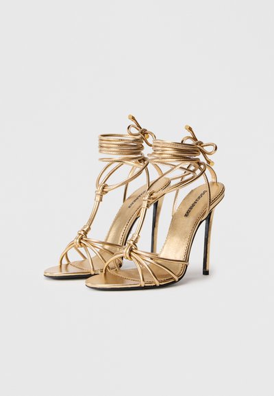 Gouden, gespen met hoge hakken sandaaltjes met knoopdetails en enkelomslag. Metalen afwerking en slanke stiletto-hak. Gladde textuur.