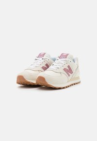 Baskets en daim beige et en mesh avec des accents roses, des lacets blancs et une semelle en caoutchouc marron. Présente le logo New Balance sur le côté et la languette.