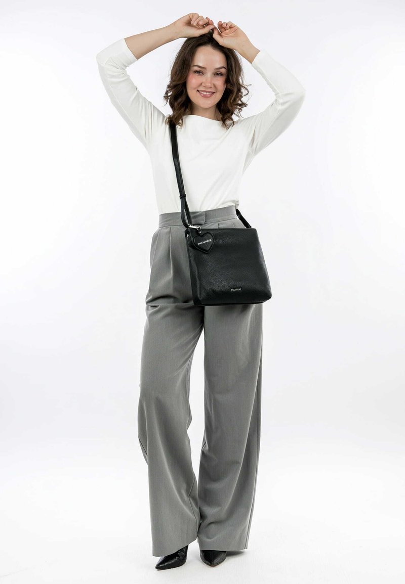 Black leather crossbody bag with a textured finish, triangular shape, adjustable strap, and a heart-shaped hardware accent.