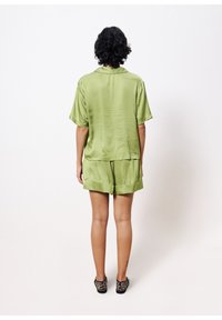 Satin grünes Kurzarmoberteil und passende Shorts, die eine lockere Passform und einen gefalteten Saum aufweisen, kombiniert mit schwarzen Schuhen im Leopardenmuster.