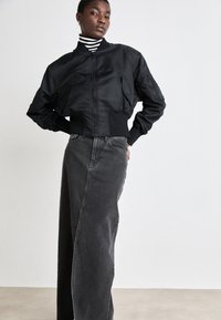Črna bomberska jakna z zadrgo spredaj, z ribanim zaključkom na rokavih in pasu. Ujemajoča visoko pasna siva jeans krila, ki ima ravno silhueto.