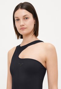 Maillot de bain noir, une épaule, avec un design découpé, texture lisse et un petit logo près du bust.