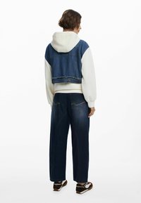 Cropped denim jacket with a white hoodie, paired with wide-leg dark denim pants. Textured, frayed edges at the jacket hem and subtle stitching details.