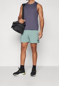 Tenue de sport comprenant un débardeur violet foncé, un short vert clair et des baskets noires avec des accents verts. Comprend un sac à bandoulière noir.