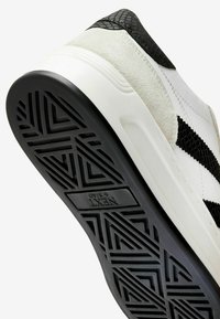 Sneaker in bianco e nero con un pannello testurizzato nero sul tallone, dettagli in camoscio e una suola in gomma con un design geometrico.