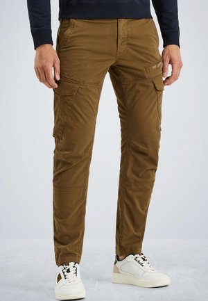 Brązowe spodnie cargo z wieloma bocznymi kieszeniami, slim fit i gładkim, lekkim materiałem. Stylizowane z białymi sneakersami dla kontrastu.