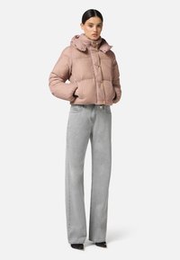 Chaqueta de plumas corta y rosa con cuello alto y botones dorados, combinada con pantalones de mezclilla gris de tiro alto y zapatos de tacón negros.