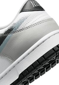 Gros plan d'une sneaker blanche et grise avec une semelle noire texturée et un détail de peinture en dégradé sur le côté près du talon.