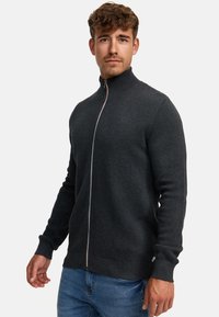 Tummanharmaa teksturoitu vetoketjullinen neule, jossa on korkea kaulus ja kontrastiväri vetoketju. Ribbaatut hihansuut ja helma, klassinen malli ja rento design.