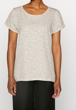 Maglietta a maniche corte di un leggero beige, con scollatura rotonda e una trama che presenta piccole macchie marroni. Indossata con pantaloni neri in satin.