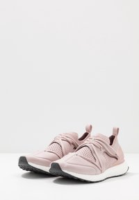 Des chaussures de sport roses avec une tige en mesh et des accents synthétiques lisses. Elles présentent des lacets élastiques, une languette au talon et une semelle en caoutchouc texturée.