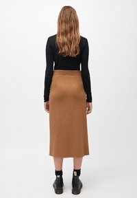 Brun stickad midi kjol med elastisk midja, slät yta och fickor med slitsar, bärs med svarta ankelboots och en svart långärmad topp.